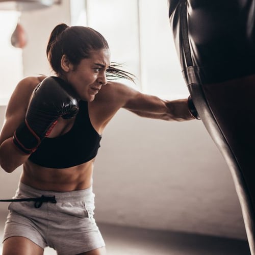 Frau boxt mit Handschuhen gegen Boxsack im Fitnessstudio, intensives Training für Kalorienverbrauch