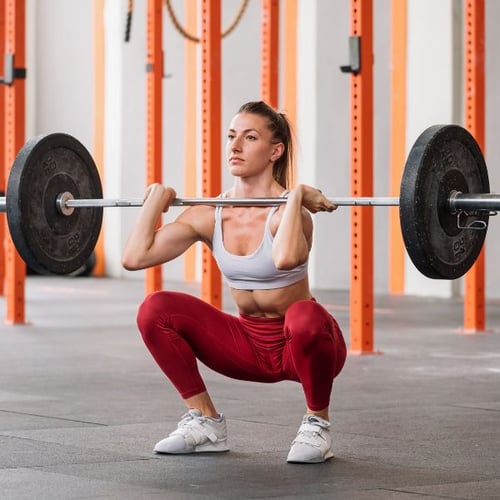 Frau macht Frontkniebeuge mit Langhantel in Fitnessstudio