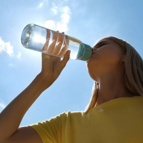 Frau trinkt Wasserflasche zur Abkühlung beim Sport bei Hitze