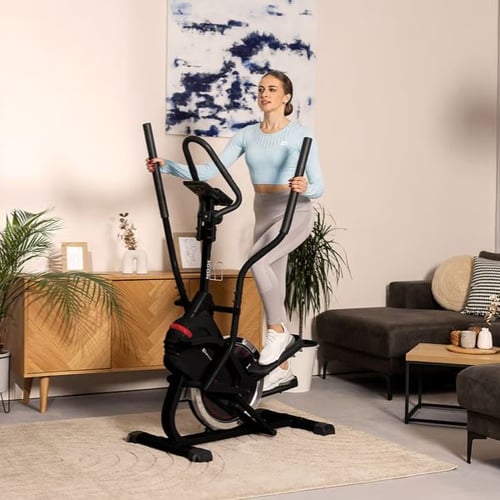 Frau trainiert auf einem Hop-Sport Crosstrainer in einem modern eingerichteten Wohnzimmer.