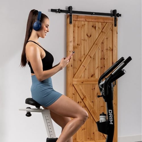 Frau trainiert auf Hop-Sport Heimtrainer und hört Musik zuhause