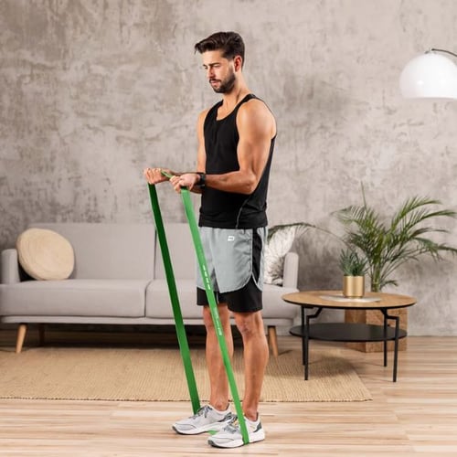 Mann macht Schultertraining mit grünem Hop-Sport Widerstandsband im Wohnzimmer