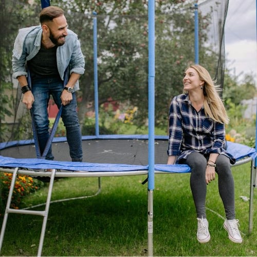 Mann lehnt sich lachend auf ein Trampolin, während eine Frau auf dem Rand sitzt.