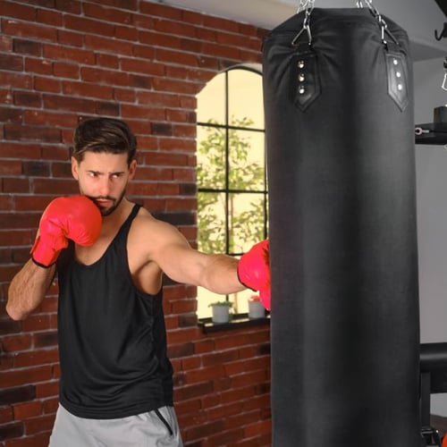 Mann mit roten Boxhandschuhen schlägt auf einen schwarzen Hop-Sport Boxsack. Er trägt ein schwarzes Tanktop und graue Shorts.