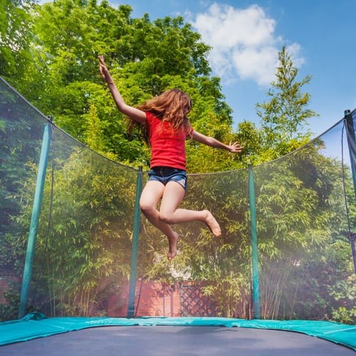 Ein Mädchen in Sommerkleidung macht Trampolin Übungen auf einer Trampolin