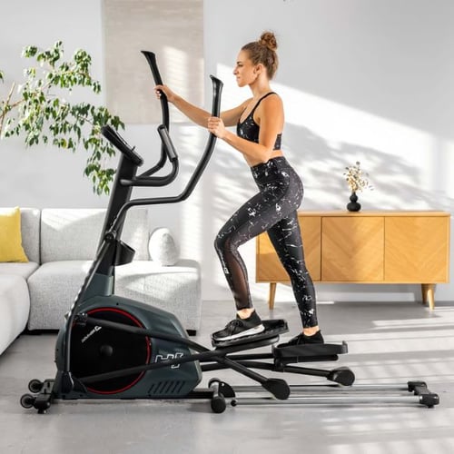 Frau trainiert auf einem Hop-Sport Crosstrainer in einem hellen, stilvollen Wohnzimmer.