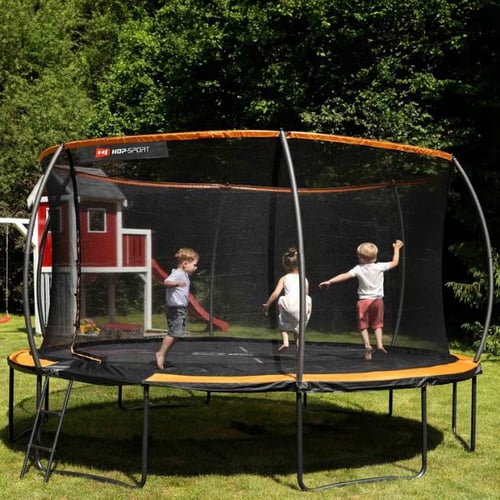 Drei Kinder hüpfen auf einem runden Trampolin von Hop-Sport mit Sicherheitsnetz. Das Trampolin steht in einem Garten mit grünem Rasen und einem Spielhaus im Hintergrund