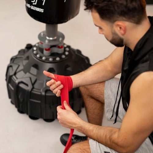 Mann bindet rote Boxbandagen vor einem Hop-Sport Stand-Boxsack