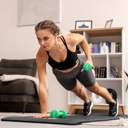 Muskelaufbau mit Kurzhanteln von Hop-Sport im Unterarmstütz auf Trainingsmatte im Wohnzimmer