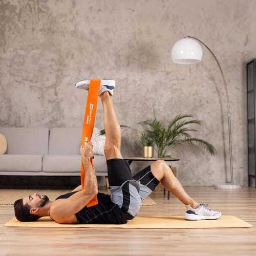 Mann dehnt Beinmuskulatur mit orangem Dehnband von Hop-Sport auf Gymnastikmatte