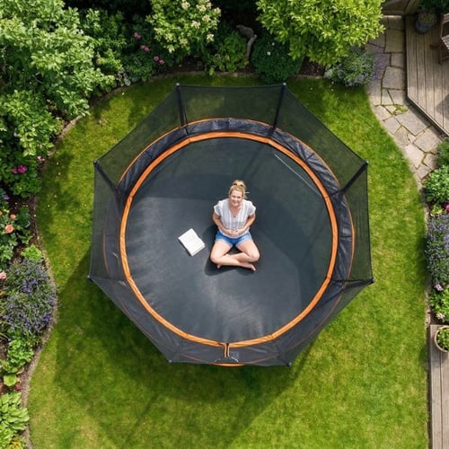 Frau sitzt auf Hop-Sport Gartentrampolin im Garten – leichtes Training auf dem Trampolin in der Schwangerschaft