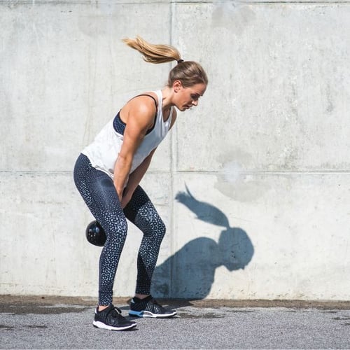 Frau führt eine Kettlebell Swing im Freien durch, trägt Sportkleidung und hält die Kettlebell in einer Schwungbewegung.