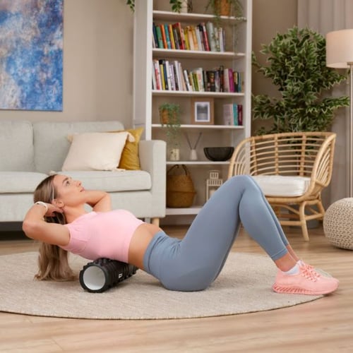 Frau macht Rückenübung mit Hop-Sport Faszienrolle auf Teppich im Wohnzimmer