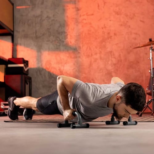 Bankdrücken Alternative: Mann führt Liegestütze mit Hop-Sport Liegestützgriffen in einem Fitnessraum durch.