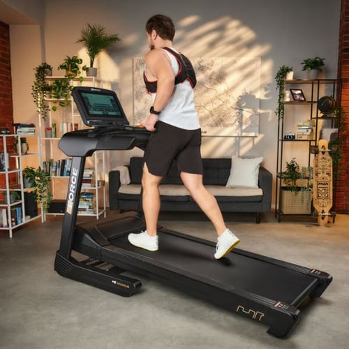 Mann joggt auf Hop-Sport Laufband mit Gewichtsweste im Wohnzimmer