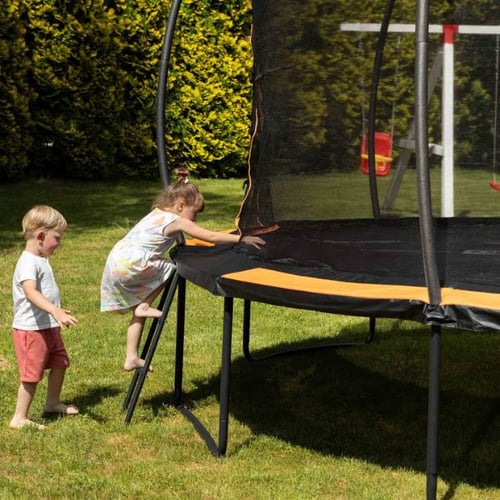 Zwei Kinder klettern auf ein Hop-Sport Trampolin mit orangefarbenem Rand und Sicherheitsnetz.