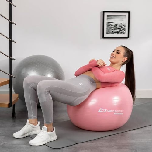 Frau trainiert unteren Rücken auf rosa Hop-Sport Gymnastikball im Homegym