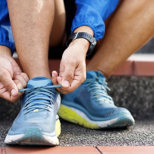 Mann schnürt blaue Laufschuhe vor dem Lauftraining