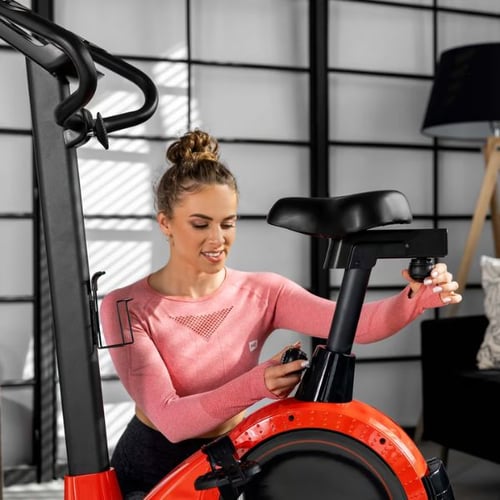 Frau justiert den Sitz eines Hop-Sport Heimtrainers mit rotem Schwungrad