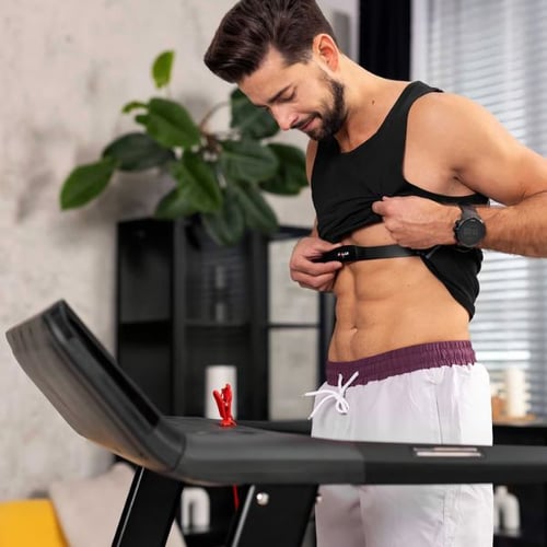 Mann befestigt Pulsgurt vor dem Laufen auf einem Hop-Sport Laufband