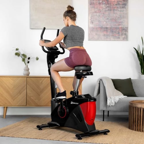 Ergometer Training zu Hause: Frau trainiert auf einem Hop-Sport Heimtrainer in Rot-Schwarz. Der Raum ist modern eingerichtet. 