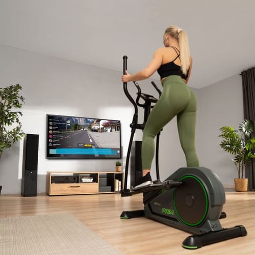 Frau trainiert rückwärts auf Hop-Sport Crosstrainer vor TV im Wohnzimmer