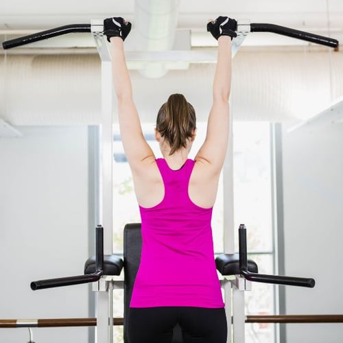 Frau beim Klimmzugtraining an einer Kraftstation, von hinten fotografiert
