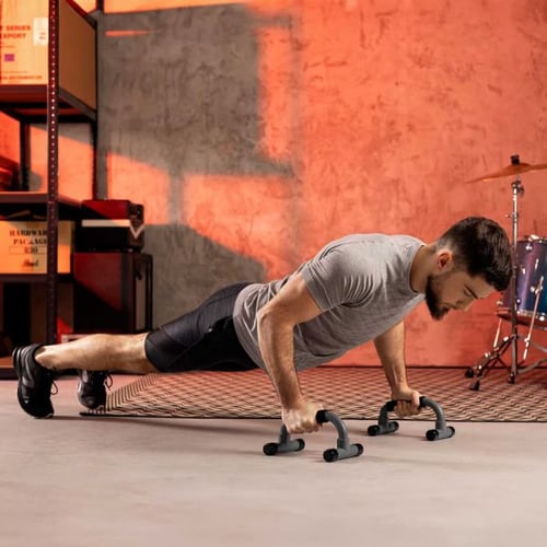 Mann trainiert mit Hop-Sport Liegestützgriffen im Fitnessraum auf einer Matte bei neutralem Hintergrund