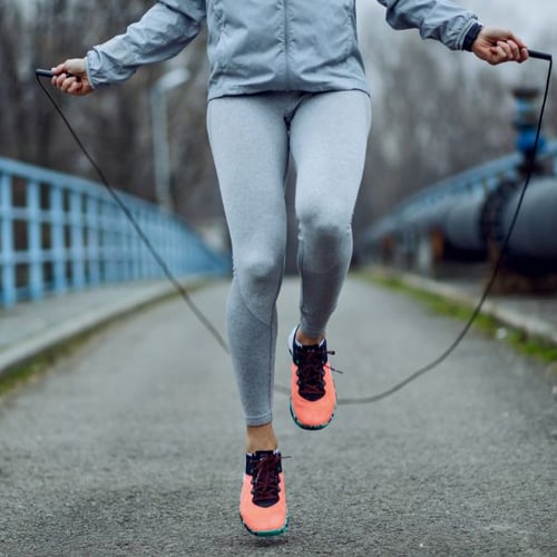 Person in grauer Sportkleidung und neonorangenen Schuhen beim Seilspringen im Freien.