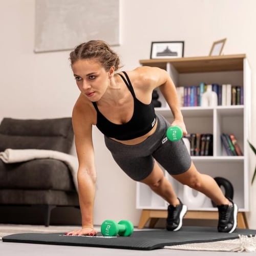 Frau macht HIIT Training mit grünen Hop-Sport Kurzhanteln im Plank zuhause