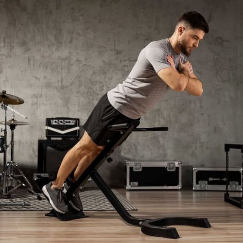 Mann trainiert auf einem Hop-Sport Hyperextensionsgerät (Rückentrainer) in einem Raum mit industriellem Look. Er trägt ein graues T-Shirt und schwarze Shorts.