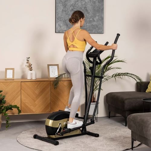 Frau trainiert auf einem Hop-Sport Crosstrainer in einem modern eingerichteten Wohnzimmer.