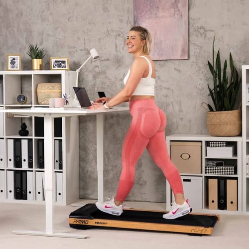 Eine Frau arbeitet an einem Stehpult, während sie auf dem Hop-Sport Laufband Primo geht. Das Laufband steht in einem modernen Büro-Wohnzimmer.