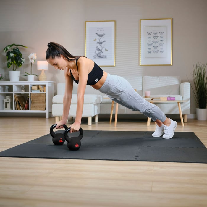 Frau trainiert im Plank mit zwei Hop-Sport Kettlebells im Home-Gym