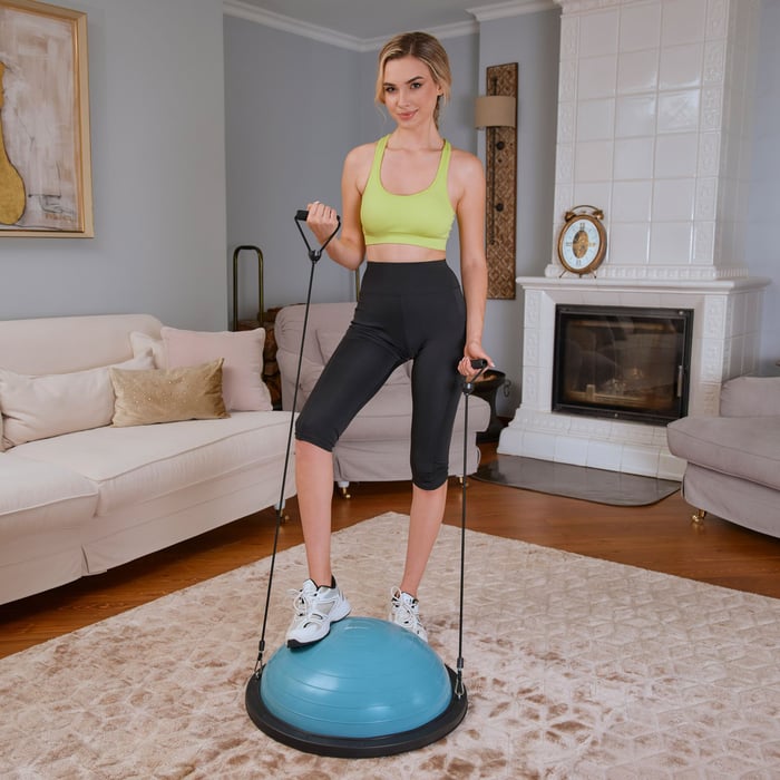 Frau führt Bizepscurls mit Widerstandsbändern auf dem Hop-Sport pastellblau Balance Trainer aus